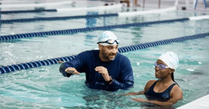 An AGUA Swim Academy instructor talking to a swimmer in the pool.
