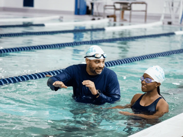 An AGUA Swim Academy instructor talking to a swimmer in the pool.