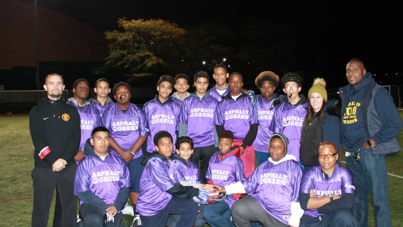 A group of people wearing matching purple jerseys poses for a photo on a field at night.