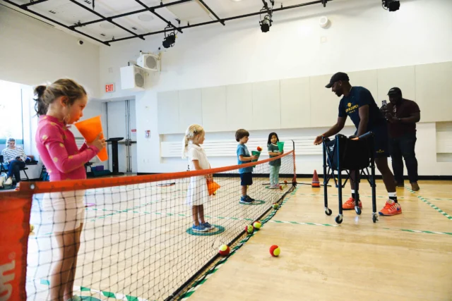 Children participate in an indoor Asphalt Green Youth Tennis class.