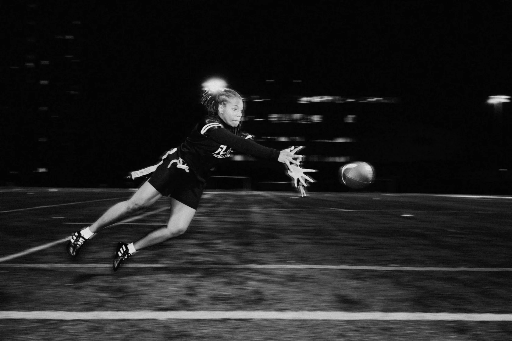 A person in athletic gear dives to catch a football on a field at night.