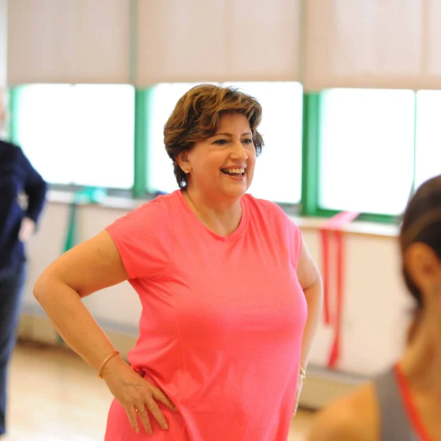Women participate in a group exercise class in a brightly lit studio, with one woman in a pink shirt smiling in the center.
