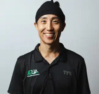 A person wearing a black collared shirt and black headband smiles at the camera against a plain light background.