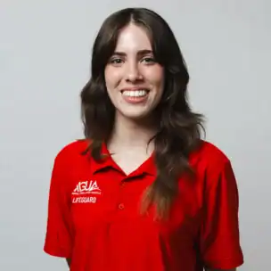 A person with long brown hair wearing a red lifeguard polo shirt smiles at the camera against a plain light background.