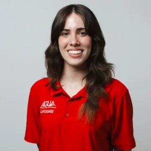 A person with long brown hair wearing a red lifeguard polo shirt smiles at the camera against a plain light background.