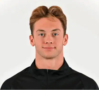 A young man with short, light brown hair wearing a black zip-up jacket, facing forward against a plain white background.