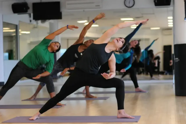 A group of people practice yoga indoors, at an Asphalt Green Fitness group exercise class.