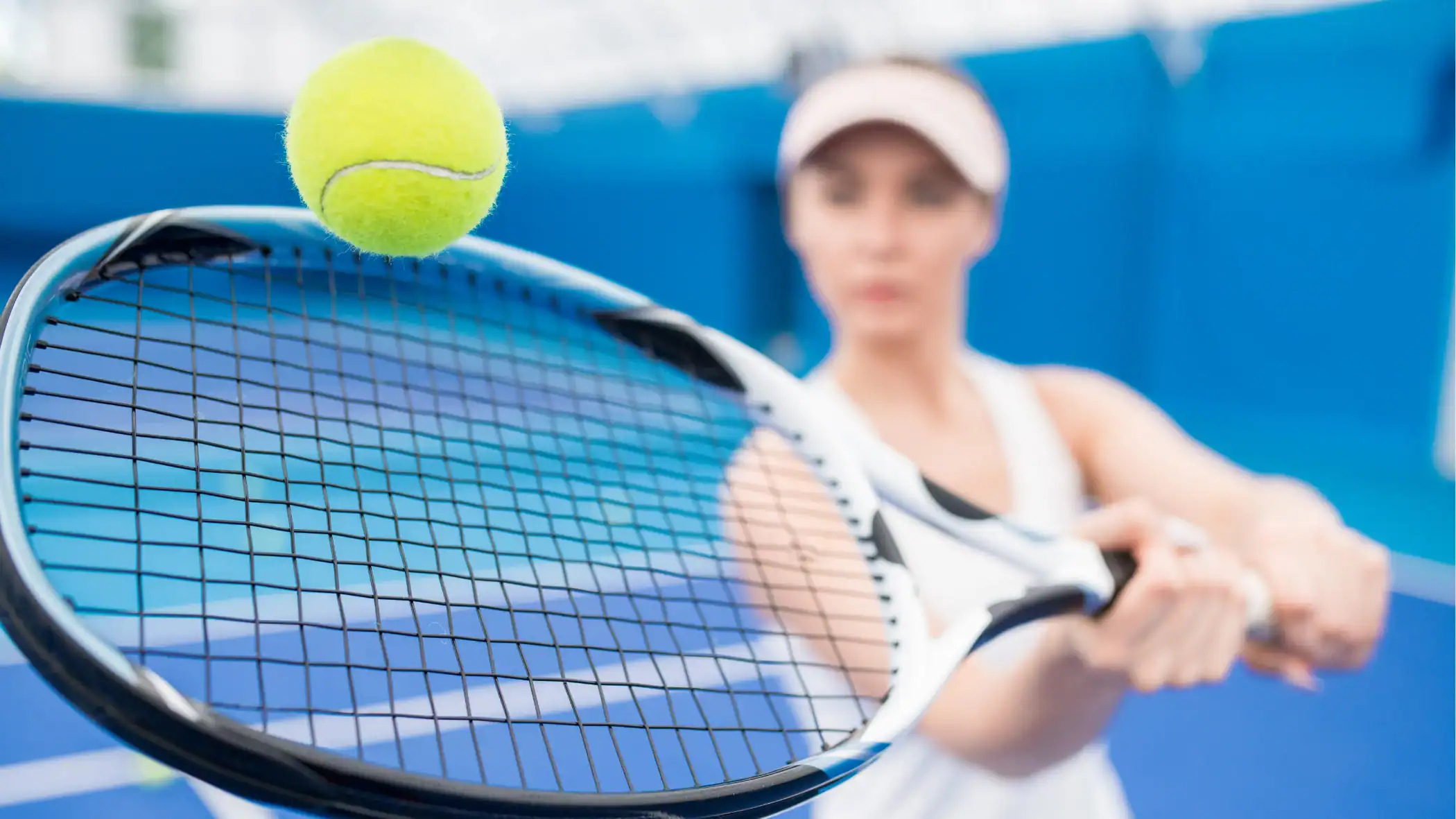 A woman in sportswear prepares to hit a tennis ball with her racket on an indoor tennis court.