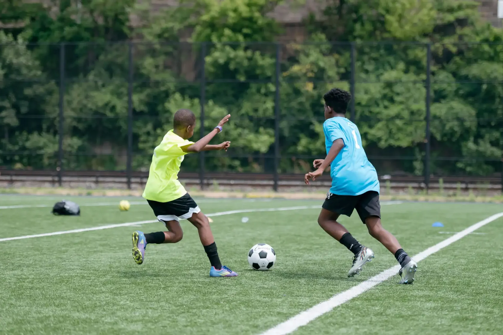 Two boys playing soccer on a field; one in a yellow jersey attempts to block the other in a blue jersey who is dribbling the ball.