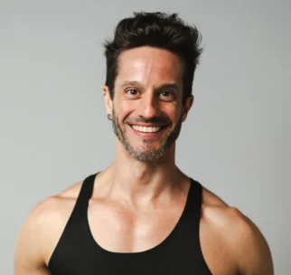 A smiling man wearing a black tank top with "AG FITNESS Asphalt Green Fitness" written on it stands against a plain background.