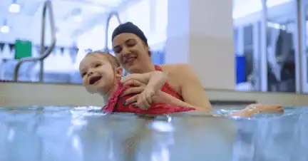 An adult holding a smiling toddler in the swimming pool.
