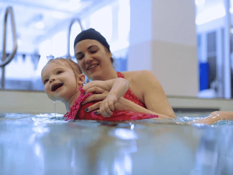An adult holding a smiling toddler in the swimming pool.