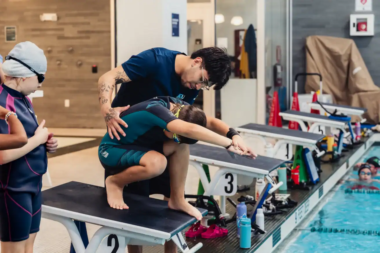 An AGUA Swim Academy instructor guiding a swimmer on proper diving form.