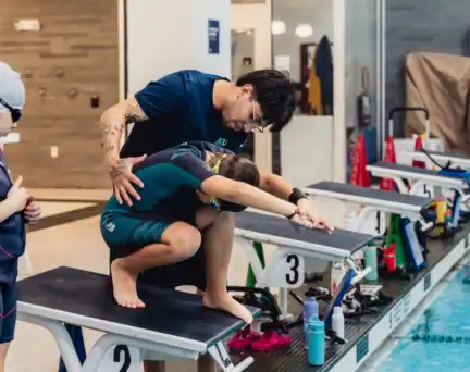 An AGUA Swim Academy instructor guiding a swimmer on proper diving form.