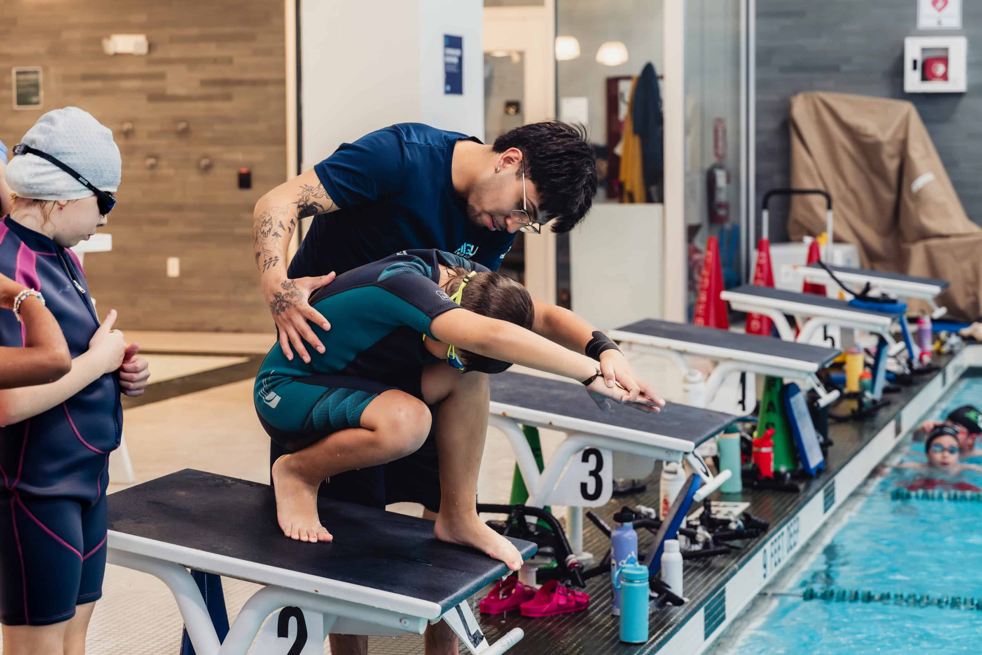 An AGUA Swim Academy instructor guiding a swimmer on proper diving form.