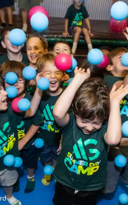 A group of children wearing “Summer Day Camp” shirts play with colorful plastic balls indoors at Asphalt Green. Photo: Jennifer Wesibord.