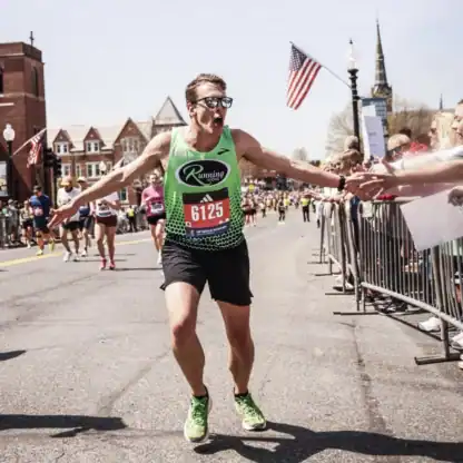 A male marathon runner with race number 6125 celebrating while reaching out to high-five spectators along the race course.