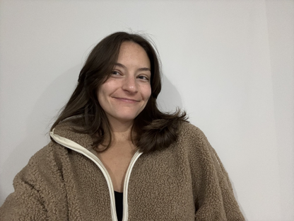 A person with shoulder-length brown hair wearing a tan fleece zip-up jacket.