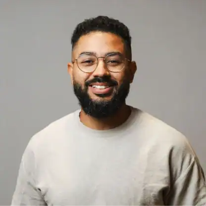 A smiling man with a beard and glasses wearing a light-colored sweatshirt.