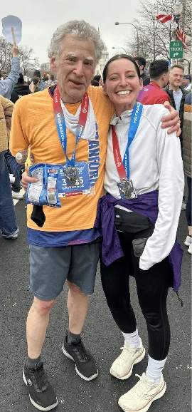 A man and a woman wearing running clothes and race medals stand together after a race.