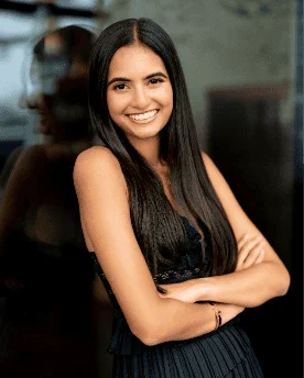 A smiling woman with long dark hair stands with her arms crossed.