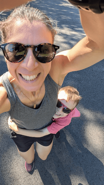 A woman wearing sunglasses takes a selfie while holding a child who is also wearing sunglasses.