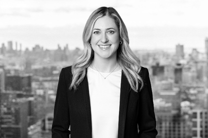 A smiling woman in a blazer stands before a city skyline.