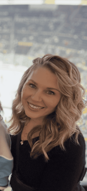 A smiling woman with blonde, wavy hair wearing a black top.