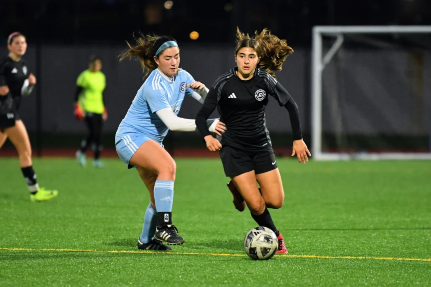 Two soccer players in opposing uniforms compete for the ball on a turf field in an inclusive sports setting.